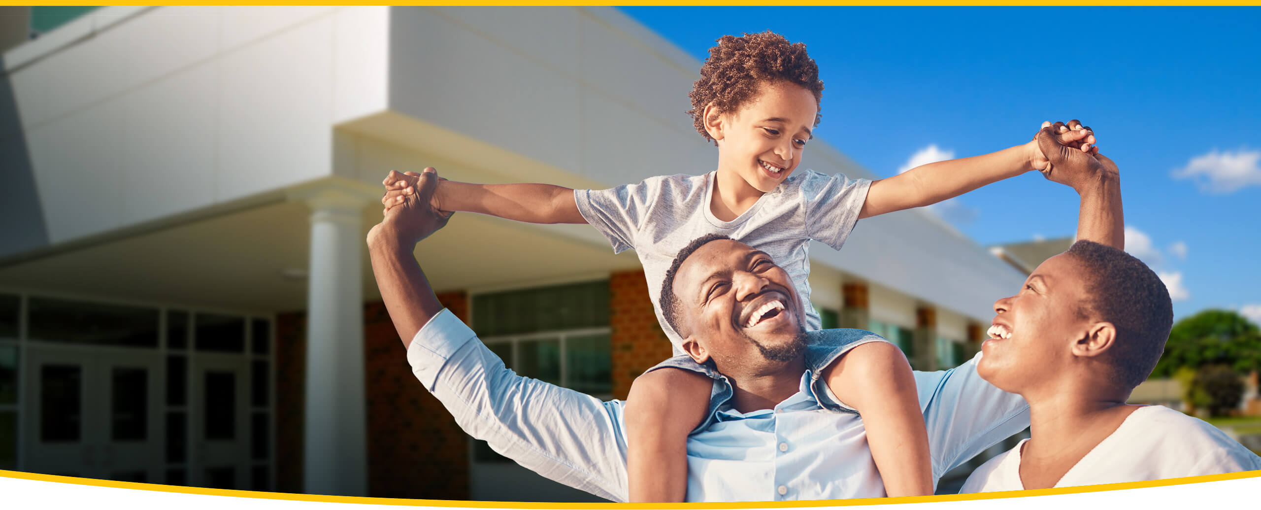 A child rides on his parents' shoulders outside a school.