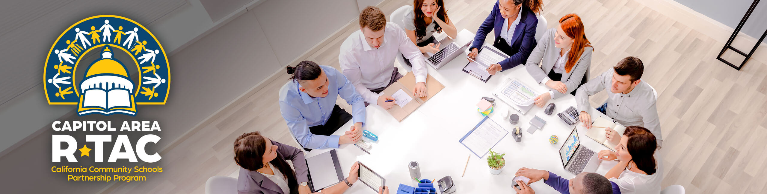 Seen from above, a diverse group of people meet around a conference table.