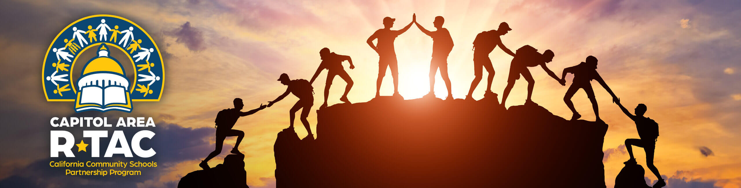 A silhouetted group of rock climbers use teamwork to reach the top.